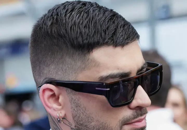 Mann mit stylischem herren kurzhaarschnitt, Sonnenbrille und Ohrringen.