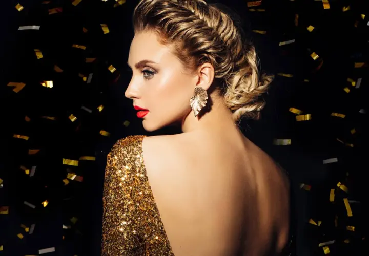 Elegante Frau mit aufwendiger Hochsteckfrisur, perfekt für Silvester-Frisuren. Goldglitzerndes Kleid und Konfetti im Hintergrund.