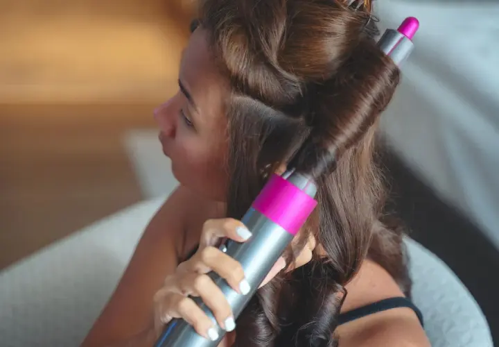 Frau stylt ihre Haare mit einem Lockenstab, um schöne Locken zu kreieren.