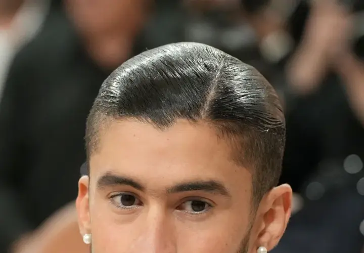 Nahaufnahme eines Mannes mit glatt zurückgekämmtem Haar und einem **low fade** Haarschnitt. Er trägt einen Perlenohrring.