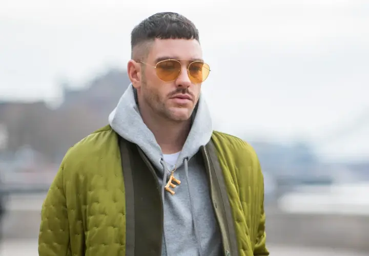 Mann mit French Crop High Fade, gelben Sonnenbrillen und Bomberjacke.