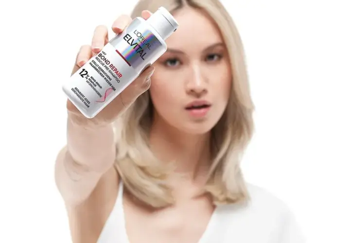 Frau hält L'Oréal Elvital Bond Repair Pre-Shampoo, um trockene Haare zu retten.