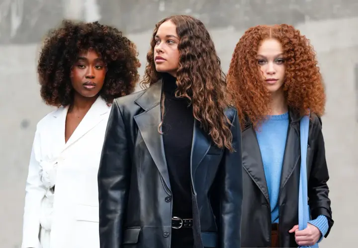Drei Frauen mit voluminösen Locken, die sich fragen, wie oft locken waschen. Eine trägt Weiß, die andere Schwarz und die dritte Blau.