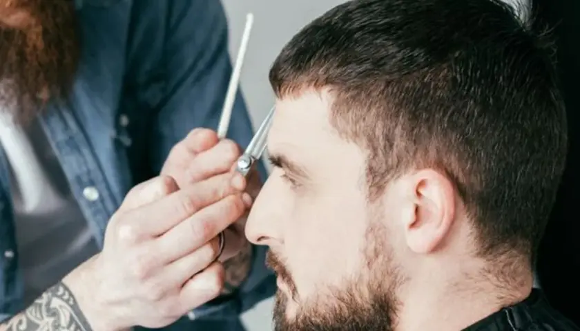 Ein Mann bekommt einen Caesar Cut. Der Friseur schneidet ihm mit einer Schere die Haare.