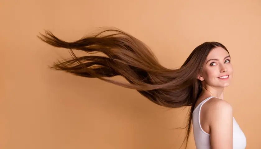 Frau mit langen, braunen Haaren, die im Wind wehen. Sie lächelt und blickt zur Seite.