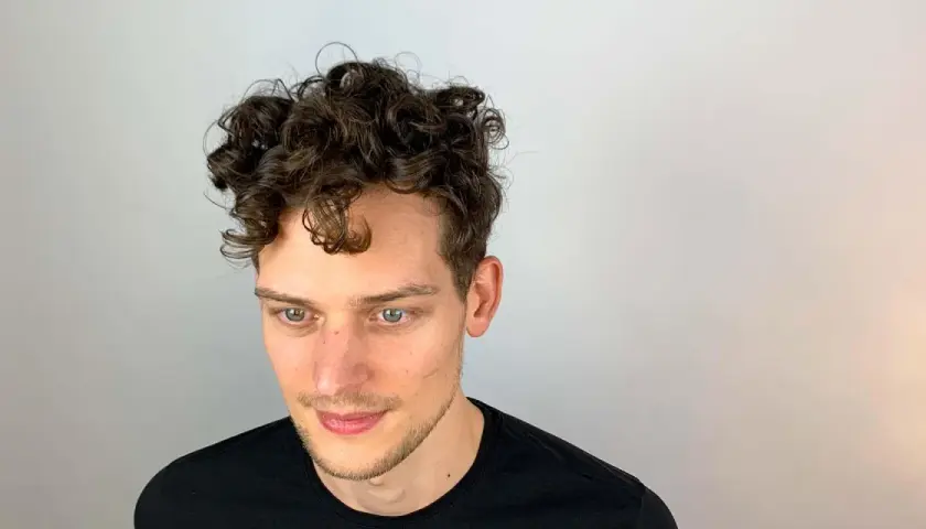 Junger Mann mit vollen, dunklen Locken. Ein Beispiel, wie bekommt man locken jungs für einen coolen Look.