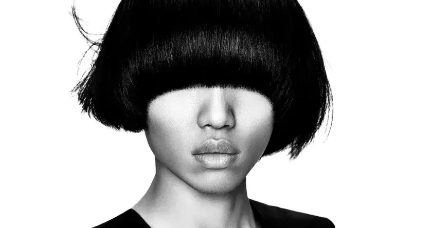 Ein Gesicht mit einem markanten **bowl cut** und dunklem Haar, das die Augen verdeckt. Die Lippen sind leicht geöffnet.