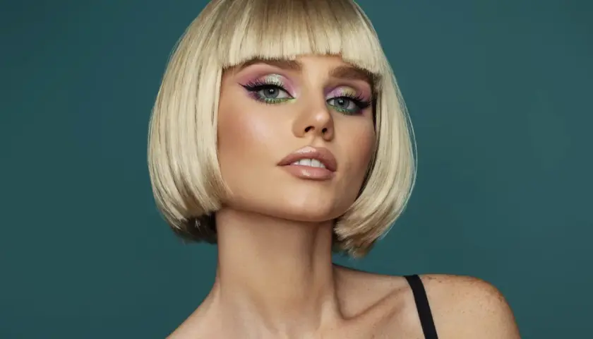 Blonde Frau mit fransig gestuftem Bob und auffälligem Make-up.