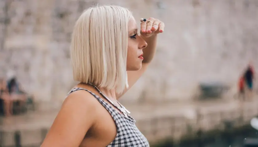 Frau mit **long bob blond** schaut in die Ferne, die Hand schützend über die Augen gelegt.
