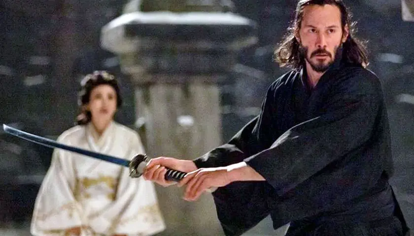 Ein Mann mit langer, dunkler Samurai-Frisur und Bart hält ein Schwert. Im Hintergrund eine Frau in weißem Kimono.