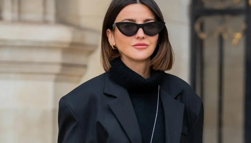 Frau mit langem Bob und Curtain Bangs, glatte Haare, trägt schwarzen Rollkragenpullover und Oversize-Blazer.