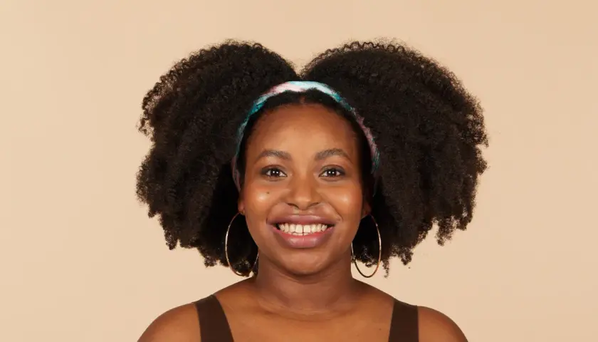 Lächelnde Frau mit voluminösen 4c Locken und einem bunten Haarband.