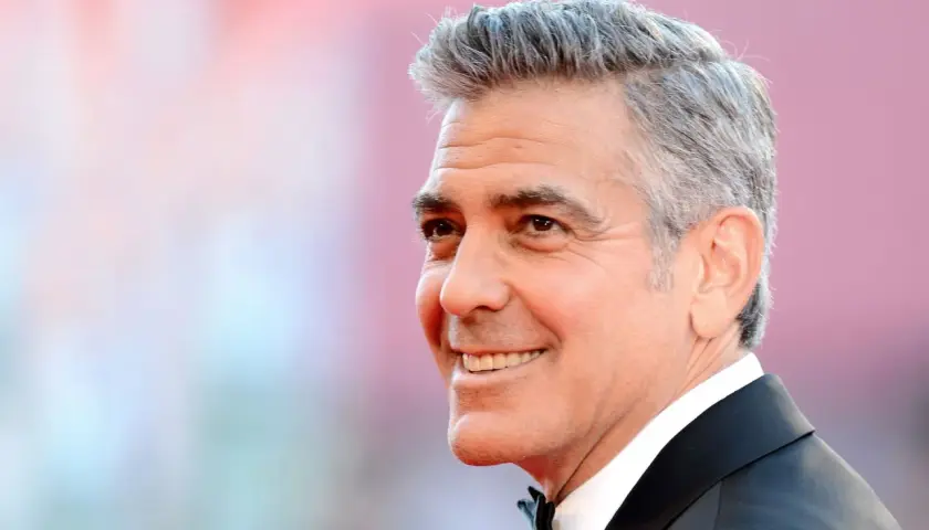 George Clooney zeigt eine stilvolle Frisur für Herren ab 60 Jahren, mit grauem Haar und einem charmanten Lächeln.