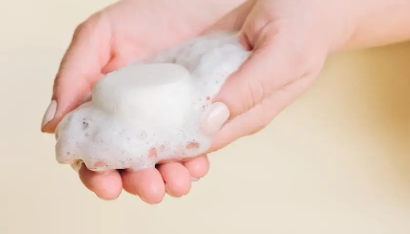 Hände halten festes Shampoo und Schaum. So einfach ist es, wie man festes Shampoo benutzt.