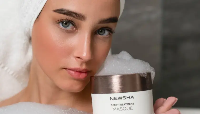 Frau mit Handtuch auf dem Kopf hält eine NEWSHA Haarmaske mit Schaum. Die Anwendung der Haarmaske verspricht Pflege.
