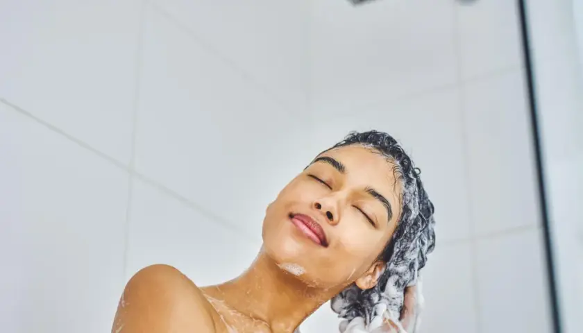 Frau genießt eine tiefenreinigende Haarwäsche unter der Dusche. Schaumige Hände massieren das Shampoo ins nasse Haar.