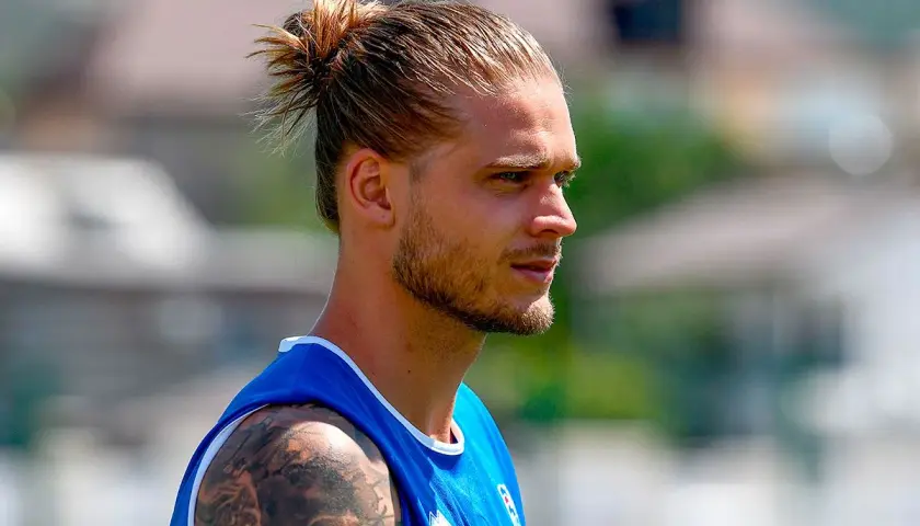 Ein Mann mit einem lässigen **man bun ohne bart**, trägt ein blaues Trikot. Sein Blick ist nach rechts gerichtet.