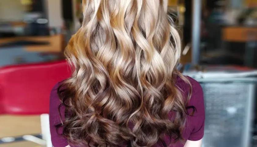 Langes, welliges Haar mit einem **Reverse Balayage**-Effekt, der von hellblond zu dunkleren Brauntönen übergeht.
