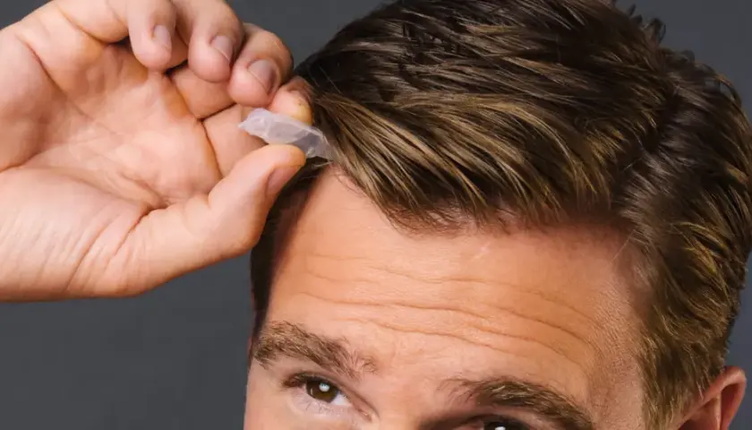 Mann mit beginnenden Geheimratsecken, der eine kleine Kapsel ins Haar drückt.