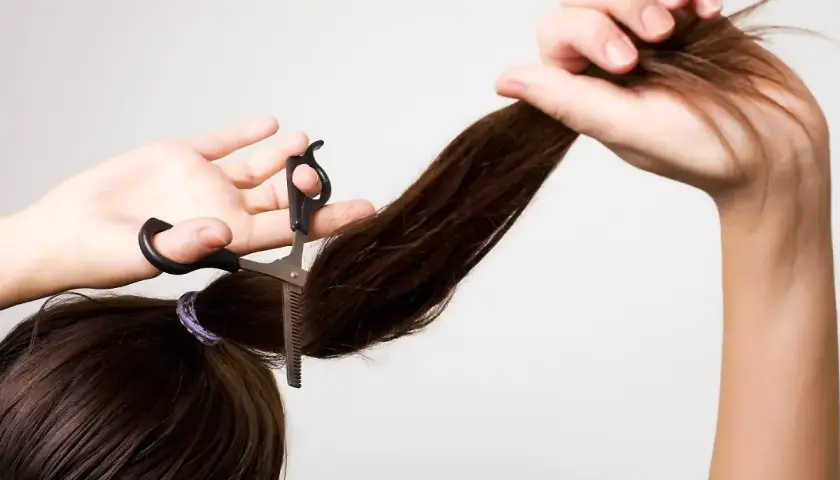 Frau schneidet sich mit einer Effilierschere die Haare, um einen Stufenschnitt selber zu schneiden.