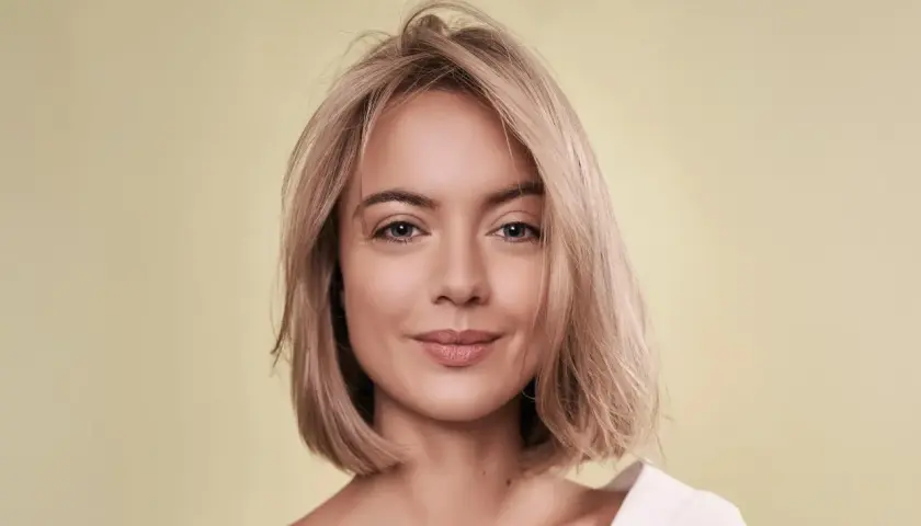 Porträt einer Frau mit blondem Haar und einem sanften Lächeln. Ihr Haar ist kurz geschnitten, wie ein **calligraphy cut**, und fällt locker um ihr Gesicht.