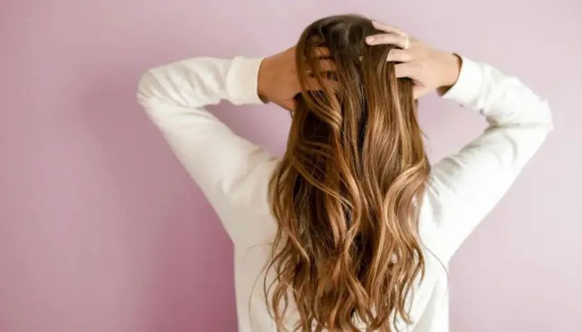 Frau mit langen, welligen 2a Haaren, die sie mit den Händen im Nacken hält.