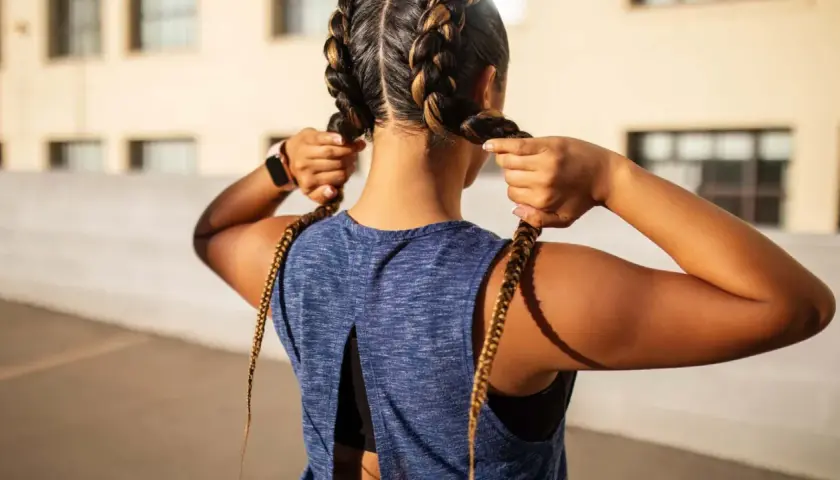 Sportliche Frau mit boxer braids, die ihre Zöpfe zurechtrückt.