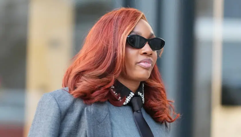 Frau mit feurigem Haar, das eine der aktuellen Haarfarben widerspiegelt, trägt Sonnenbrille und grauen Blazer.