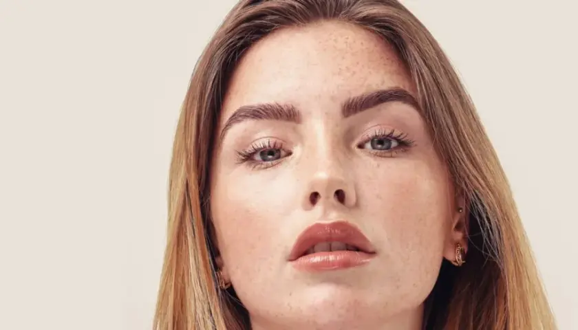 Nahaufnahme einer jungen Frau mit Sommersprossen und dunkelblond hellbraunen Haaren, die sanft über ihre Schultern fallen.