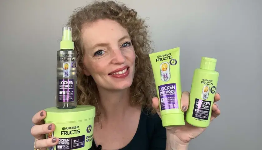 Frau mit lockigem Haar präsentiert die Garnier Fructis Locken Methode Produkte: Shampoo, Pre-Shampoo und Feuchtigkeits-Spray für definierte Locken.