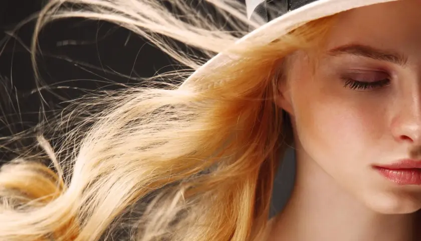 Ein Mädchen mit feinen Haaren, die im Wind wehen, trägt einen Hut.