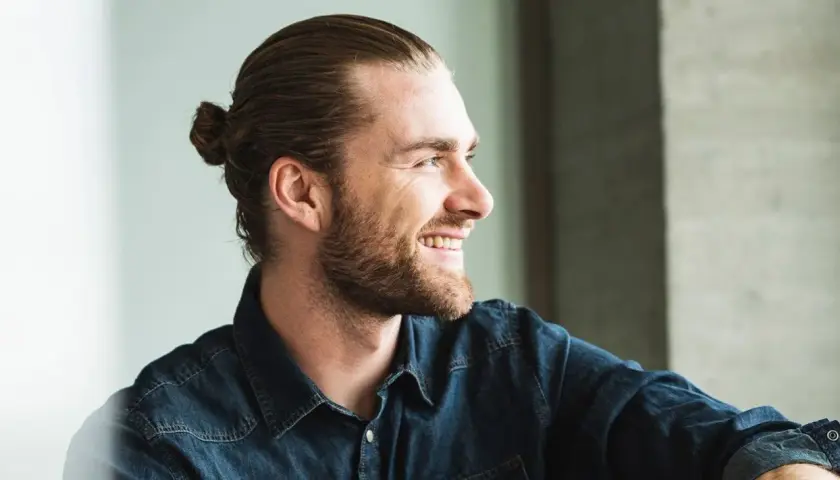 Lächelnder Mann mit Bart und einem lässigen **man bun** im Jeanshemd.
