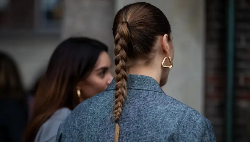 Eine Frau mit geflochtenen Haaren trägt einen grauen Blazer und auffällige goldene Ohrringe.