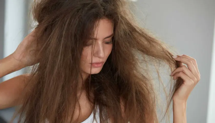 Frau mit zerzaustem Haar, das sich trocken anfühlt. Ihre trockene Haarspitzen sind sichtbar, als sie nachdenklich ihr Haar berührt.
