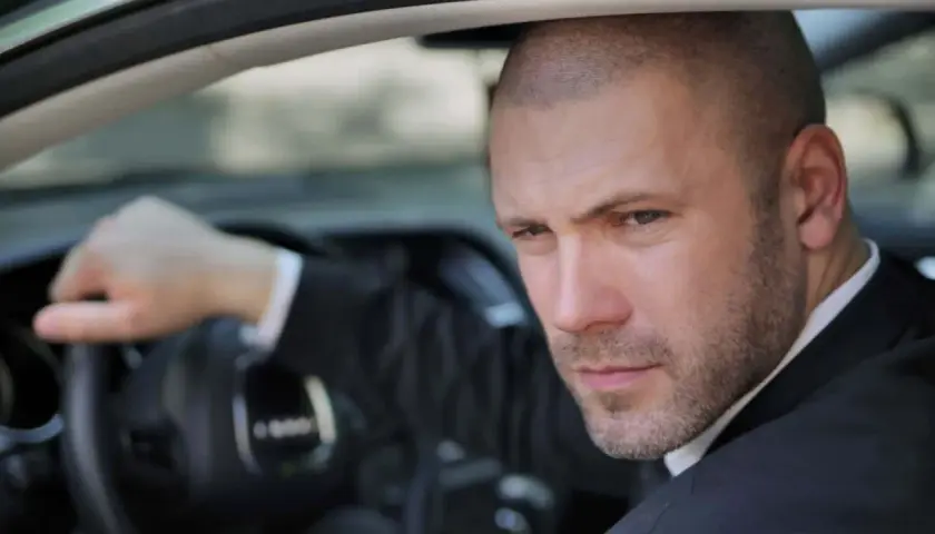Mann mit Buzz Cut Mid Fade im Anzug fährt Auto.