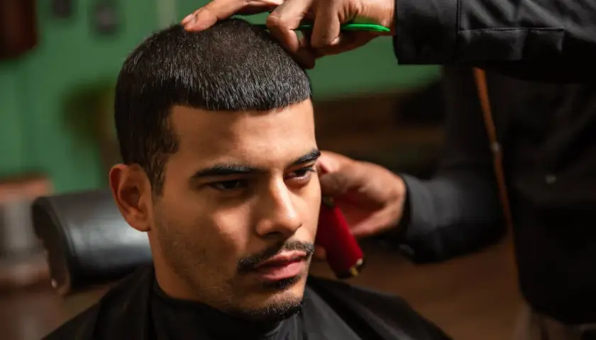 Mann bekommt einen Buzz Cut 15mm. Der Friseur trimmt das Haar mit einer Schere und einem Trimmer.