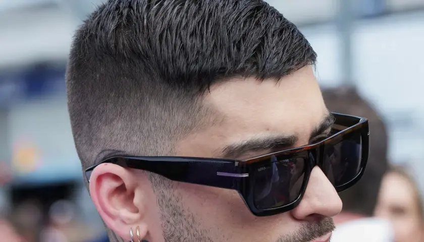 Mann mit stylischem herren kurzhaarschnitt, Sonnenbrille und Ohrringen.