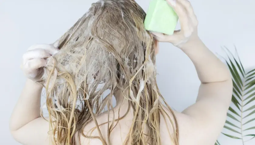 Frau wäscht sich die Haare mit einem festen Shampoo-Riegel. Die Herstellung von Shampoo kann so einfach sein.