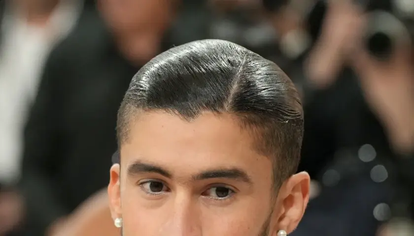 Nahaufnahme eines Mannes mit glatt zurückgekämmtem Haar und einem **low fade** Haarschnitt. Er trägt einen Perlenohrring.