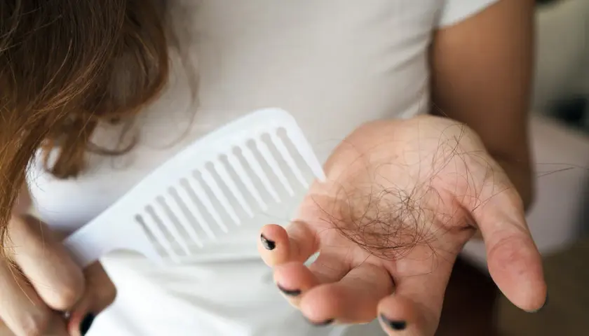 Frau hält Haarkamm und eine Handvoll Haare, die auf extremer Haarausfall nach Schwangerschaft hindeuten.