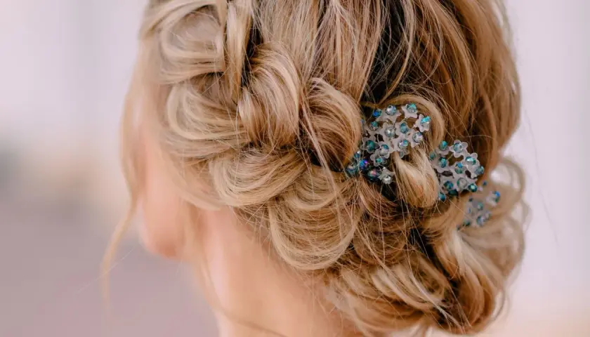 Zarte, geflochtene Strähnen und lockere Wellen ergeben eine elegante Hochsteckfrisur, verziert mit funkelnden Haarschmuck. Einfach und doch raffiniert.