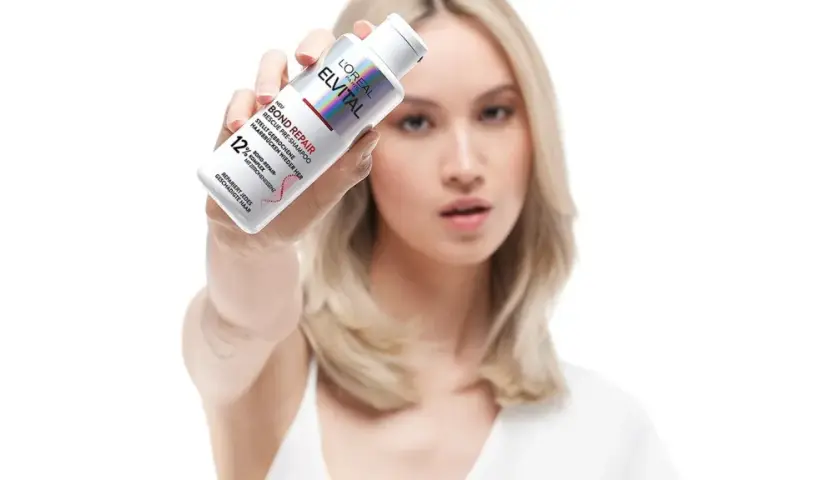 Frau hält L'Oréal Elvital Bond Repair Pre-Shampoo, um trockene Haare zu retten.