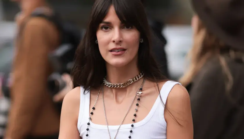 Frau mit dunklem Haar und Curtain Bangs, die eine weiße Tanktop und Chanel-Schmuck trägt.