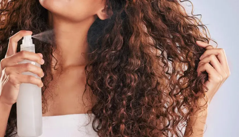 Frau sprüht ihr volles, lockiges Haar mit einem Spray ein, um die Definition der Curly Methode zu verbessern.