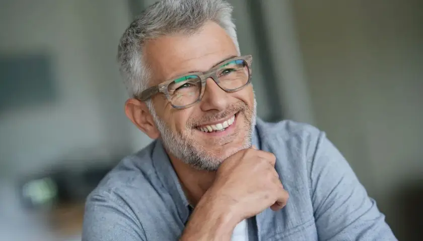 Lächelnder Mann mit Brille und grauem Haar, ein Beispiel für moderne herren frisuren ab 50.