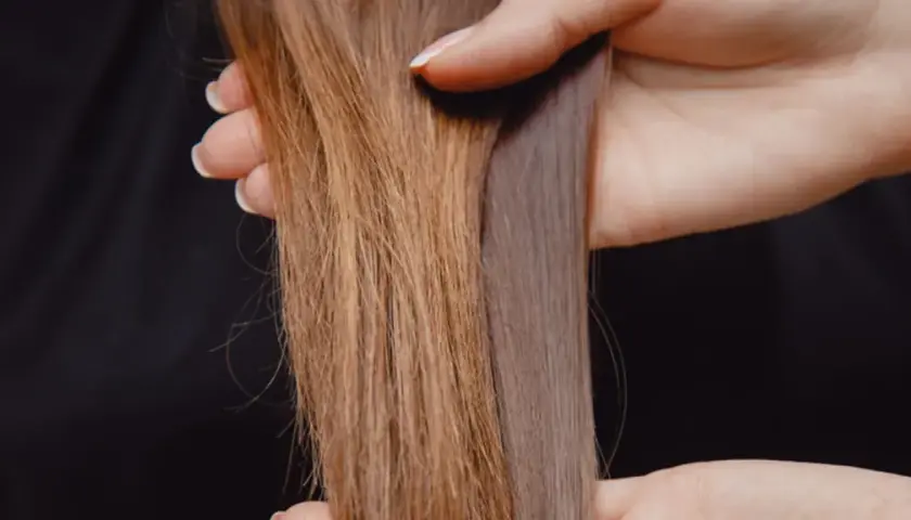 Hände halten zwei Strähnen lange Haare, eine braun, die andere grau-violett.