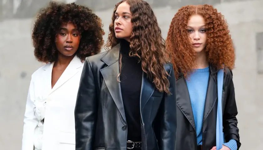 Drei Frauen mit voluminösen Locken, die sich fragen, wie oft locken waschen. Eine trägt Weiß, die andere Schwarz und die dritte Blau.