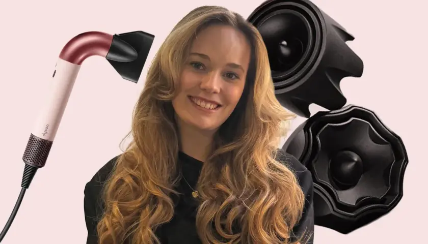 Lächelnde Frau mit voluminösen, welligen Haaren, die durch einen Dyson-Haartrockner und schwarze Aufsätze betont werden. Die Konturen der Haare sind perfekt gestylt.
