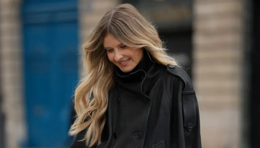 Frau mit blonden Haaren, die einen schwarzen Leder-Trenchcoat trägt. Ihre Haare haben einen schönen Ombre-Look, der an "Ombre selber machen" erinnert.