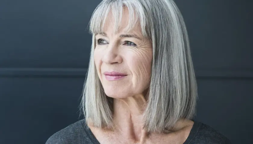 Porträt einer Frau mit stilvollen grauen Haaren, die nachdenklich zur Seite blickt.
